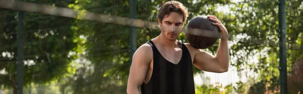 Brunette sportsman holding basketball ball near blurred fence, banner — Stock Photo