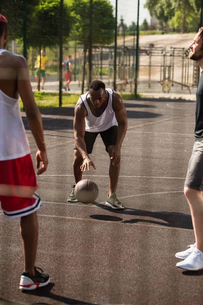 Africano americano hombre jugando baloncesto cerca borrosa amigos al aire libre - foto de stock