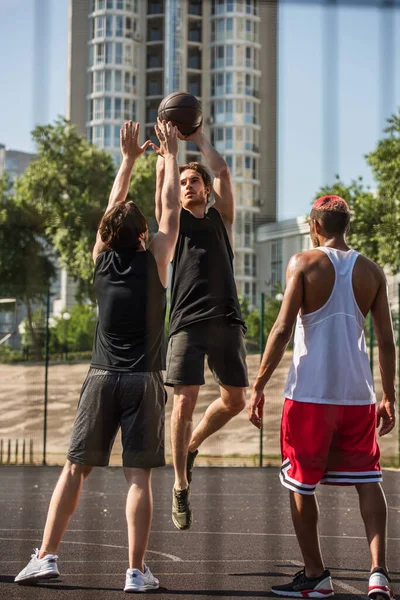 Sportsman with basketball ball jumping near interracial sportsmen outdoors — Stock Photo