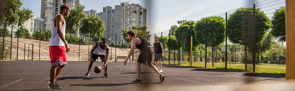 Jóvenes deportistas multiétnicos jugando baloncesto cerca de amigos al aire libre, pancarta - foto de stock
