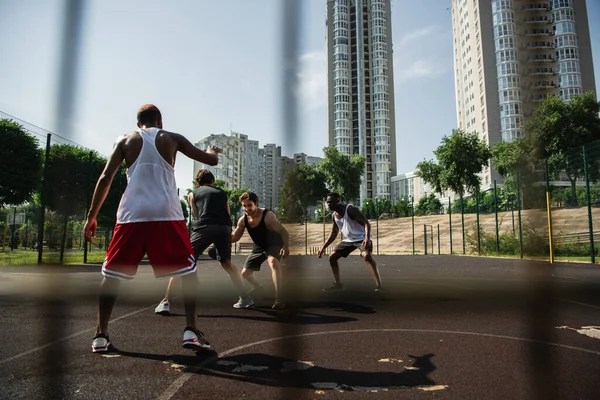 Young multiethnic men playing basketball on playground on urban street — Stock Photo