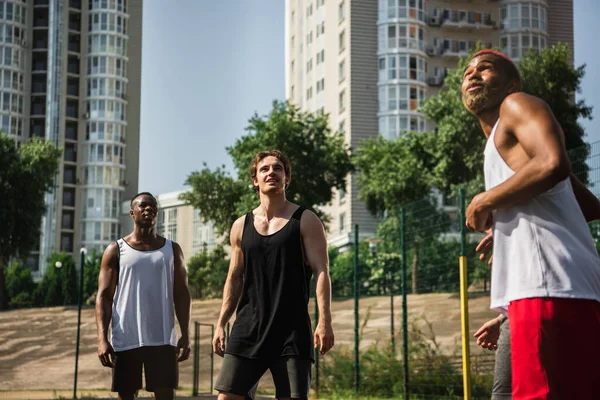 Positive interracial sportsmen looking away outdoors — Stock Photo