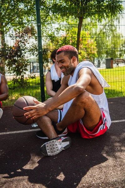 Sorridente uomo africano americano che tiene palla da basket vicino agli amici sul parco giochi — Foto stock