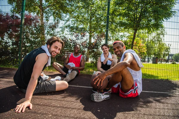 Heureux sportifs multiethniques regardant la caméra sur le terrain de basket-ball — Photo de stock