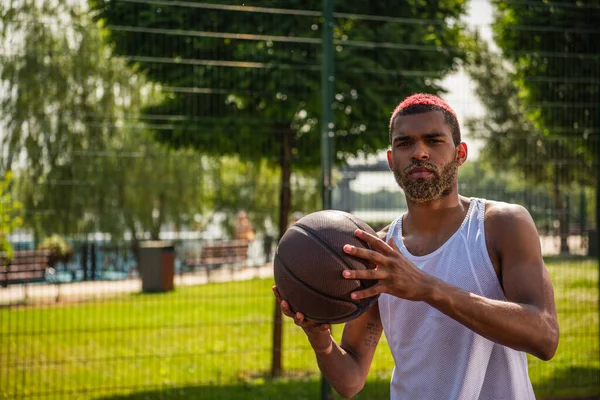 Афроамериканський спортсмен з баскетбольним м'ячем дивиться на камеру на вулиці — стокове фото