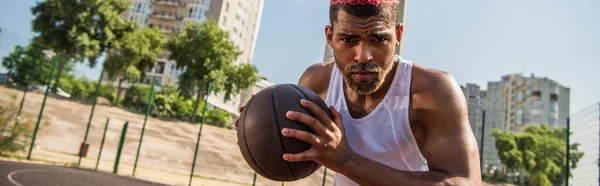 Afroamerikaner hält Basketball auf verschwommenem Spielplatz im Freien, Banner — Stockfoto