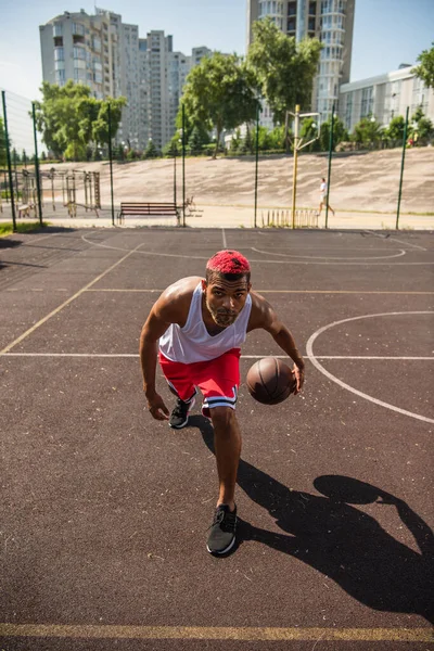 Молодой американский спортсмен с окрашенными волосами играет в баскетбол на детской площадке — стоковое фото