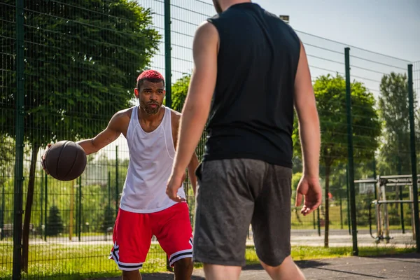 Afroamerikanischer Sportler mit Basketballball schaut während eines Wettkampfes verschwommenen Spieler an — Stockfoto