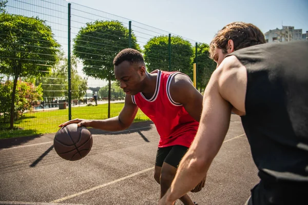 Uomo afroamericano che gioca a basket con un amico offuscato nel parco giochi — Foto stock