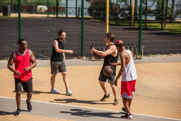 Deportistas interracial positivos con pelotas de baloncesto hablando al aire libre — Stock Photo