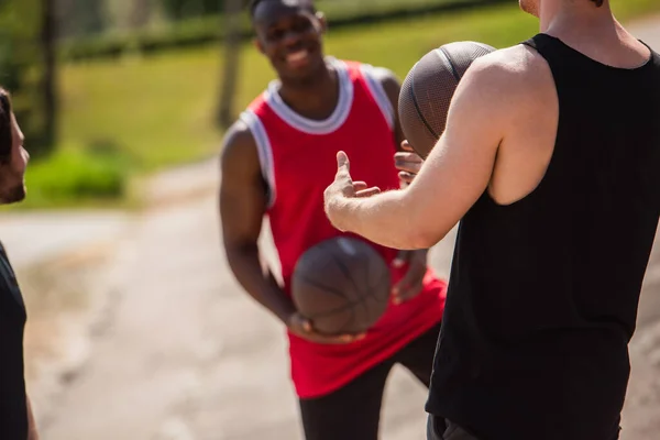 Esportista segurando bola de basquete perto de amigos inter-raciais borrados ao ar livre — Fotografia de Stock