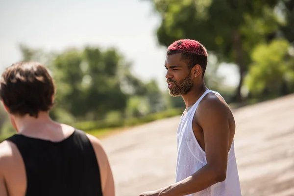 Afro americano deportista hablando cerca borrosa amigo al aire libre - foto de stock