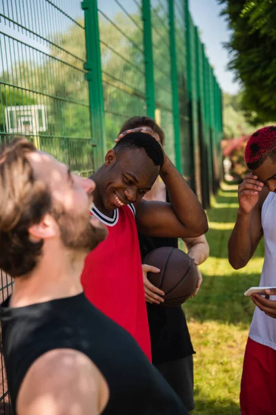 Міжрасові баскетболісти з м'ячем і смартфоном сміються на відкритому повітрі — стокове фото