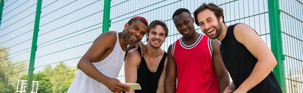 Міжрасові спортсмени зі смартфоном посміхаються на камеру на відкритому повітрі, банер — стокове фото