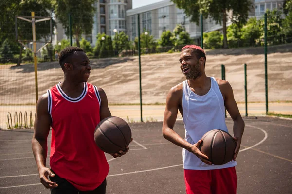 Sonrientes jugadores de baloncesto afroamericanos caminando por el patio de recreo - foto de stock