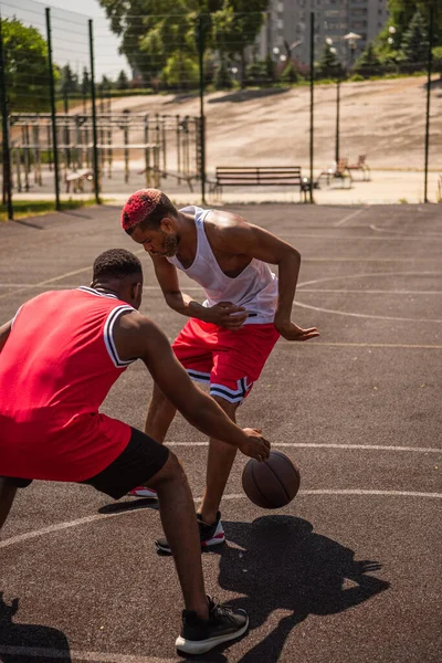 Jóvenes deportistas afroamericanos jugando baloncesto en la cancha durante el día - foto de stock