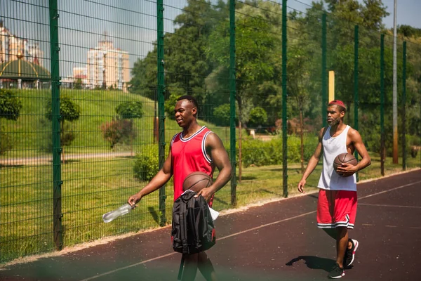 Jugadores de baloncesto afroamericanos con pelotas y agua caminando en el parque infantil - foto de stock