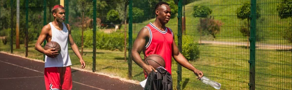 Des sportifs afro-américains avec des balles de basket et de l'eau marchant sur l'aire de jeux, bannière — Photo de stock