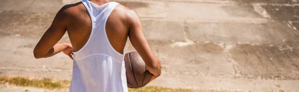 Vista cortada do homem americano africano segurando bola de basquete ao ar livre, bandeira — Fotografia de Stock