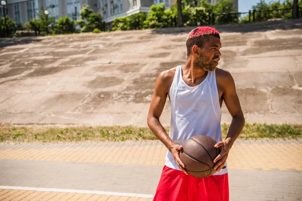 Vue latérale d'un sportif afro-américain tenant un ballon de basket à l'extérieur — Photo de stock