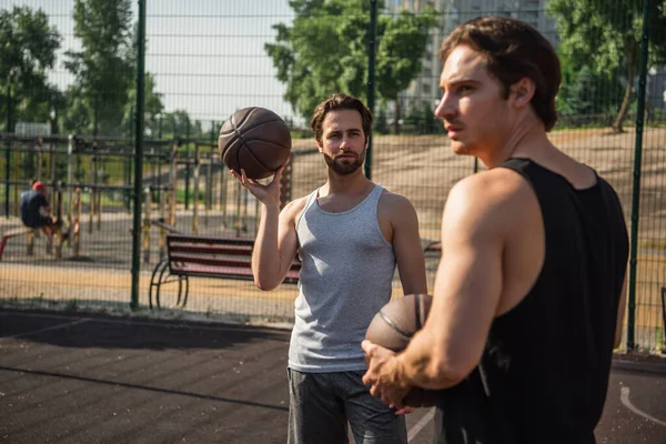 Hombre sosteniendo pelota de baloncesto cerca borrosa amigo en el patio de recreo - foto de stock