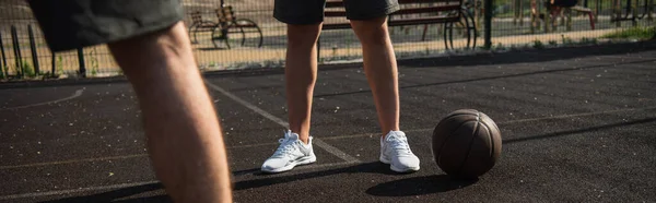 Vista ritagliata dello sportivo in piedi vicino alla palla da basket sul parco giochi, banner — Foto stock