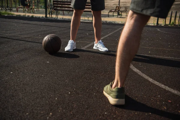 Обрізаний вид на спортсменів, що стоять біля баскетбольного м'яча на корті — стокове фото