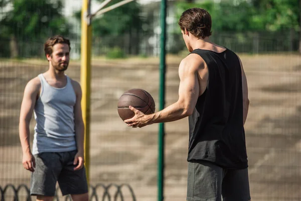 Uomo atletico che tiene palla da basket vicino amico offuscata all'aperto — Foto stock