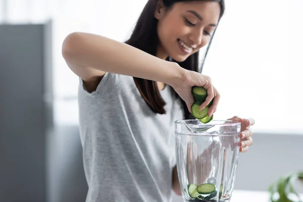 Verschwommene asiatische Frau lächelt, während sie Gurkenscheiben in den Mixer gibt — Stockfoto