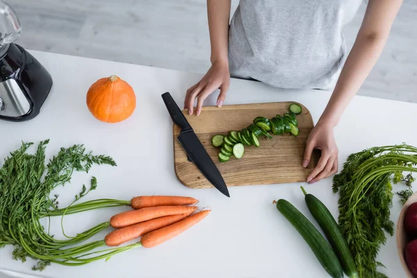 Vue partielle de la femme près de la planche à découper avec concombre tranché, carottes et citrouille sur la table — Photo de stock