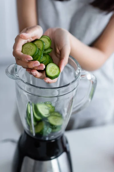 Vue recadrée de femme floue ajoutant concombre coupé dans shaker électrique — Photo de stock