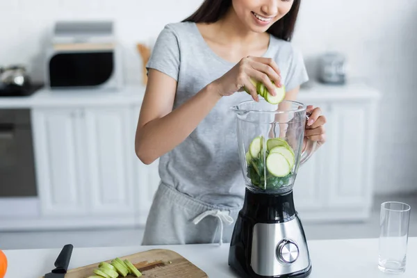 Abgeschnittene Ansicht einer lächelnden Frau, die geschnittene Zucchini in einen elektrischen Shaker gibt — Stockfoto