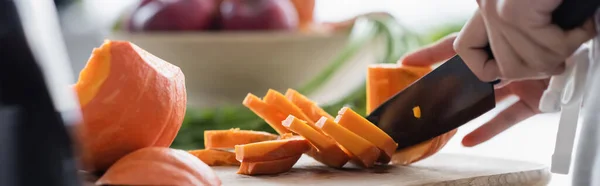 Vue partielle de femme coupant mûre, citrouille fraîche sur planche à découper, bannière — Photo de stock