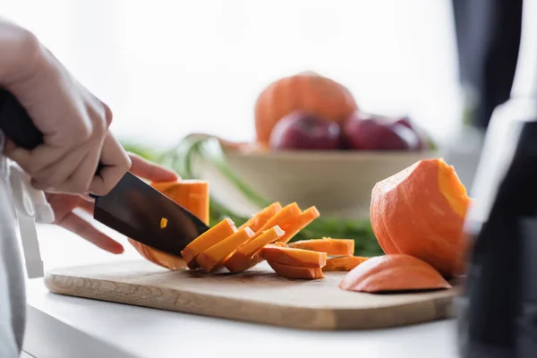 Vue partielle de femme coupant la citrouille crue sur la planche à découper dans la cuisine — Photo de stock