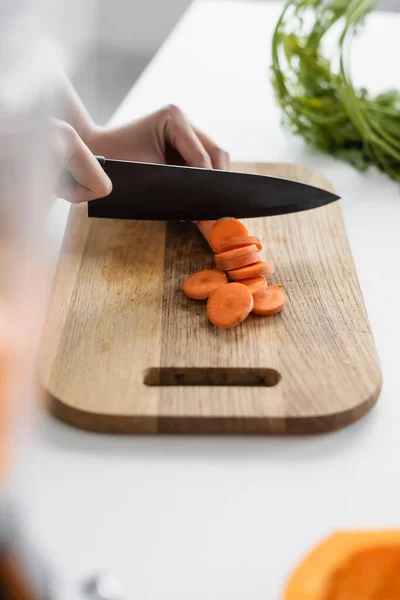 Cropped view of woman cutting fresh carrot on chopping board, blurred foreground — Stock Photo