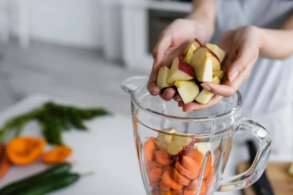 Visão cortada de mulher adicionando maçãs em jarro de liquidificador com cenouras cortadas — Fotografia de Stock