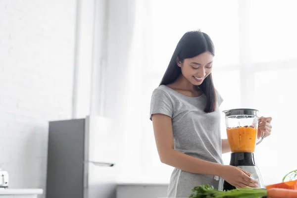 Cheerful asian woman preparing vegetable smoothie for breakfast in kitchen — Stock Photo