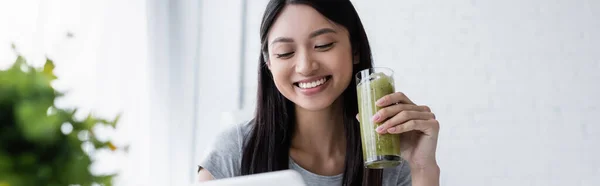 Hübsche asiatische Frau lächelt, während sie ein Glas leckeren Smoothie hält, Banner — Stockfoto