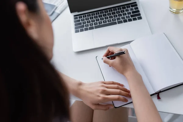 Visão parcial da mulher desfocada escrevendo no notebook perto do laptop na mesa — Fotografia de Stock