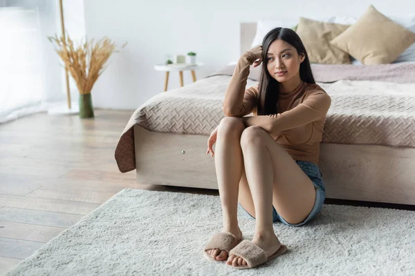 Junge asiatische Frau schaut weg, während sie auf dem Fußboden im Schlafzimmer sitzt — Stockfoto