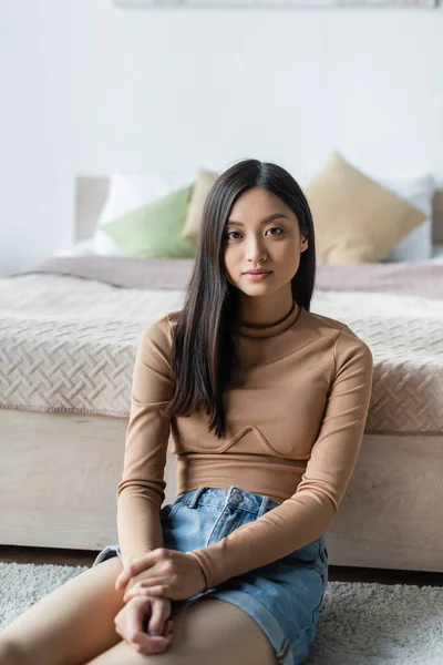 Junge asiatische Frau sitzt in der Nähe des Bettes und schaut in die Kamera — Stockfoto