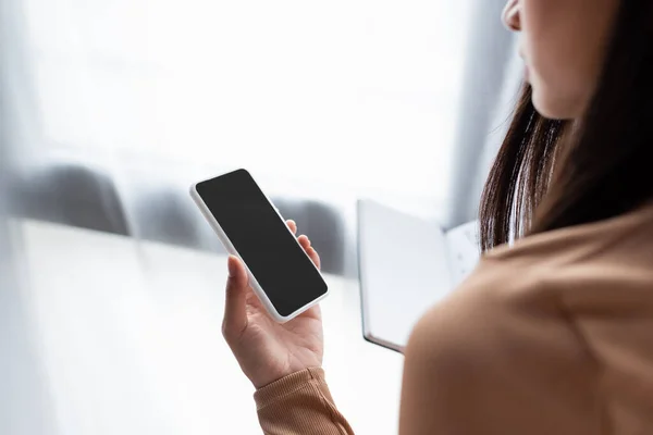 Vista parcial de la mujer sosteniendo el teléfono móvil con pantalla en blanco - foto de stock