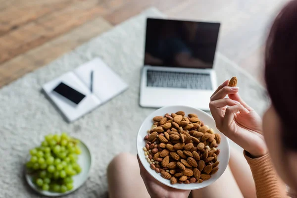 Vista recortada de la mujer comiendo almendras cerca de aparatos borrosos y uva fresca en el suelo - foto de stock