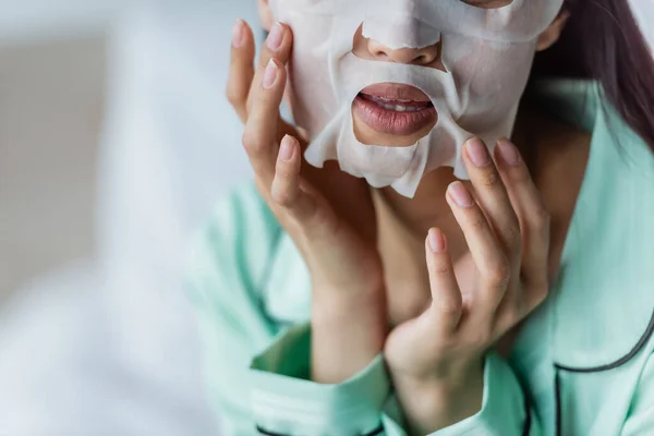 Vista recortada de la mujer que aplica la máscara de hoja en la cara en casa - foto de stock
