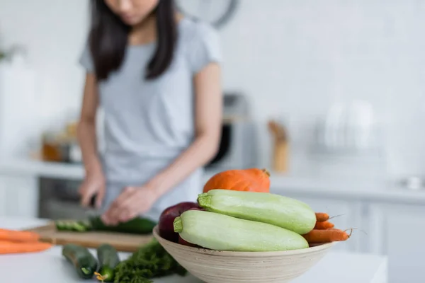 Selective focus of bowl with fresh vegetables near blurred woman preparing breakfast, cropped view — Stock Photo