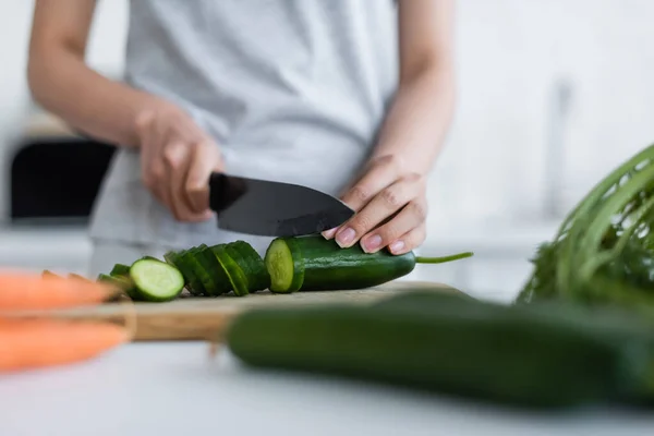 Partial view of woman cutting fresh cucumber on blurred foreground — Stock Photo