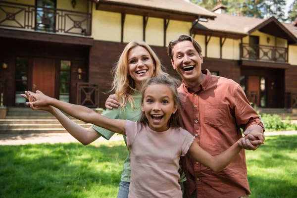 Cheerful kid looking at camera near parents and vacation house — Stock Photo