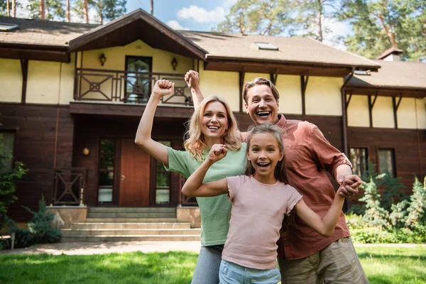 Emocionada familia mostrando sí gesto cerca de la casa de vacaciones - foto de stock