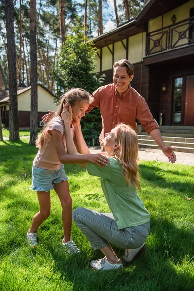 Усміхнена мати торкається дочки біля чоловіка на газоні — стокове фото