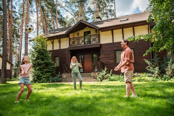 Позитивна сім'я грає у волейбол на галявині біля будинку відпочинку — стокове фото